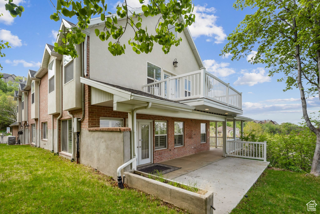 Rear view of house featuring a balcony, brick siding, stucco siding, a yard, and central AC unit