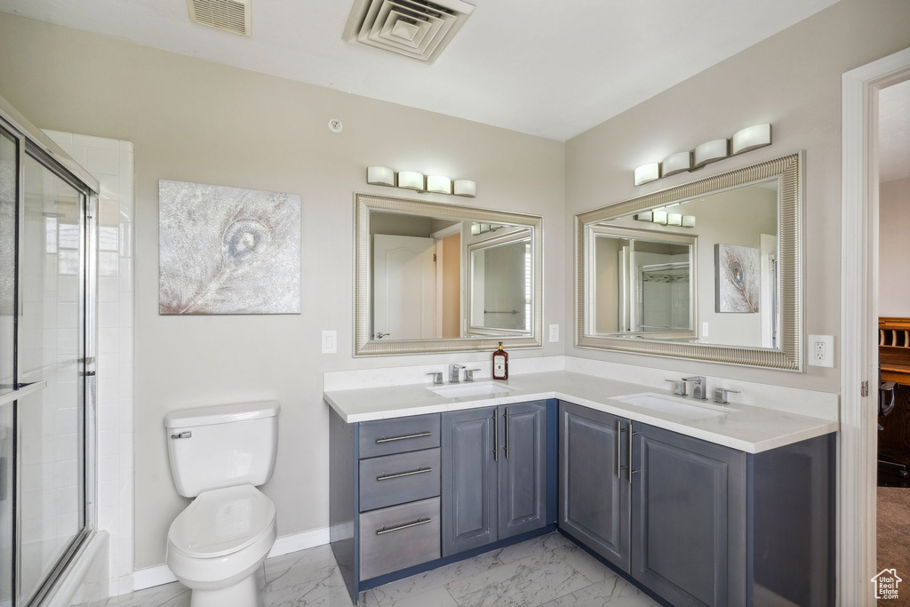 Full bath featuring marble look tiles, an enclosed shower, double vanity, toilet, and baseboards
