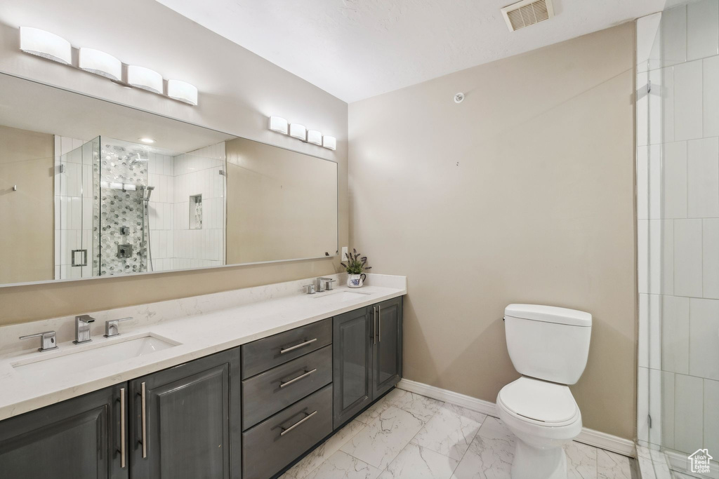 Bathroom with marble look tiles, toilet, a shower stall, baseboards, and double vanity