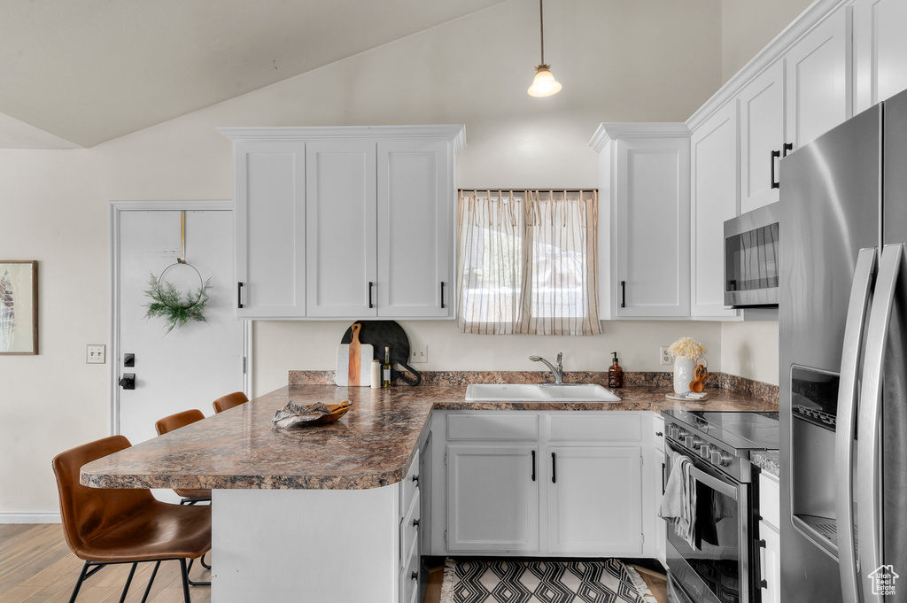 Kitchen featuring stainless steel appliances, a sink, vaulted ceiling, a kitchen bar, and white cabinetry