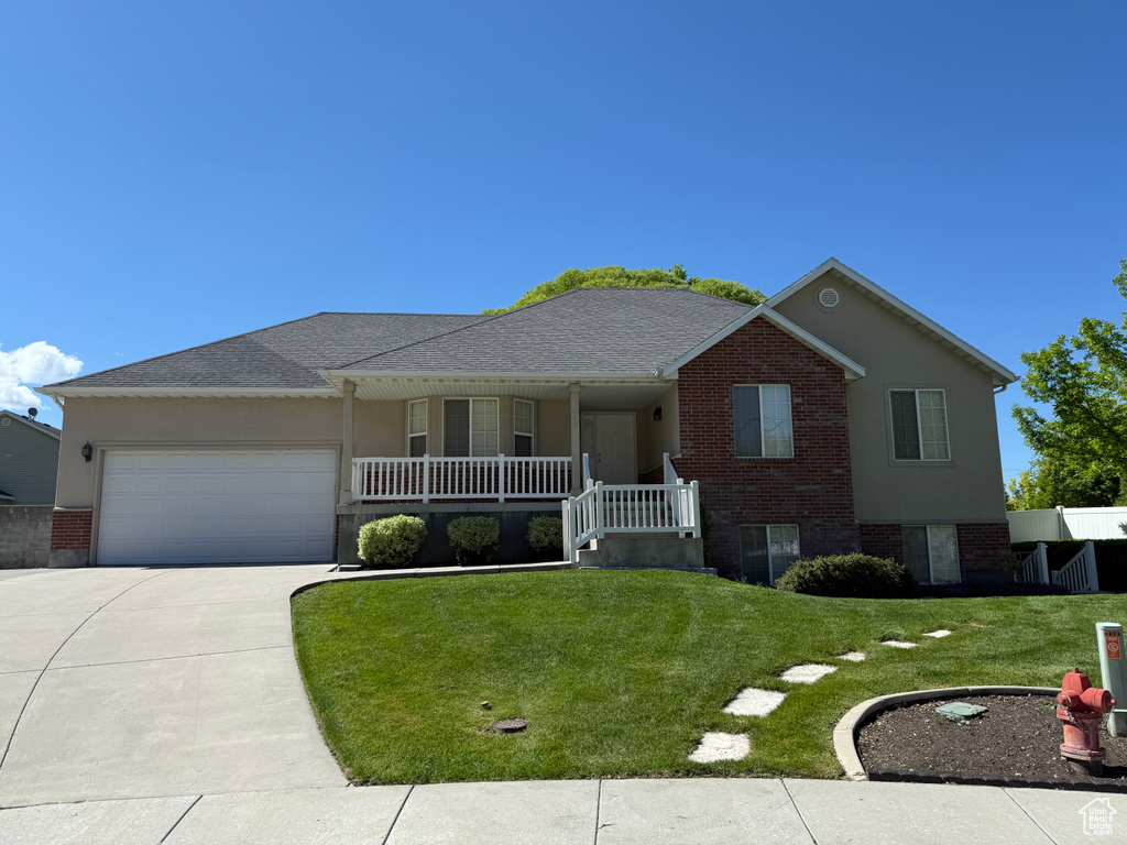 Ranch-style house featuring an attached garage, covered porch, driveway, a front lawn, and brick siding