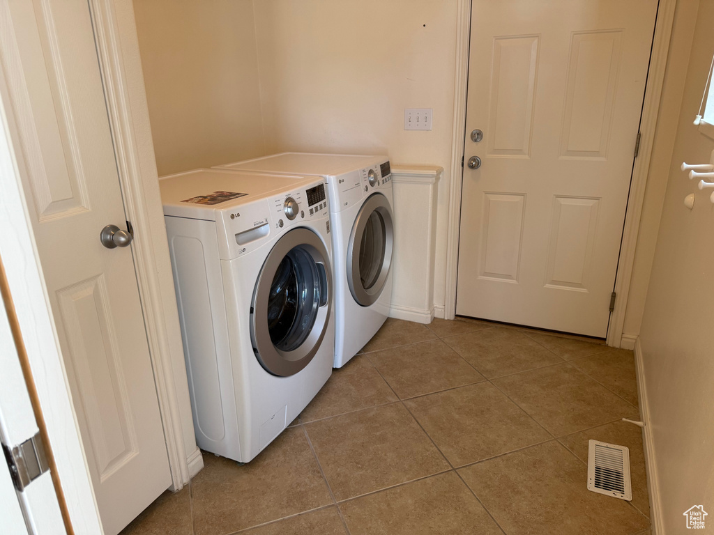 Washroom with washing machine and clothes dryer and light tile patterned floors