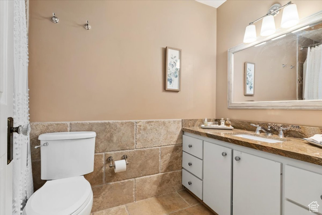 Full bathroom featuring tile walls, a wainscoted wall, toilet, vanity, and a shower with shower curtain