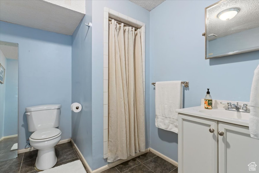 Full bath featuring a textured ceiling, tile patterned flooring, toilet, vanity, and a shower with curtain