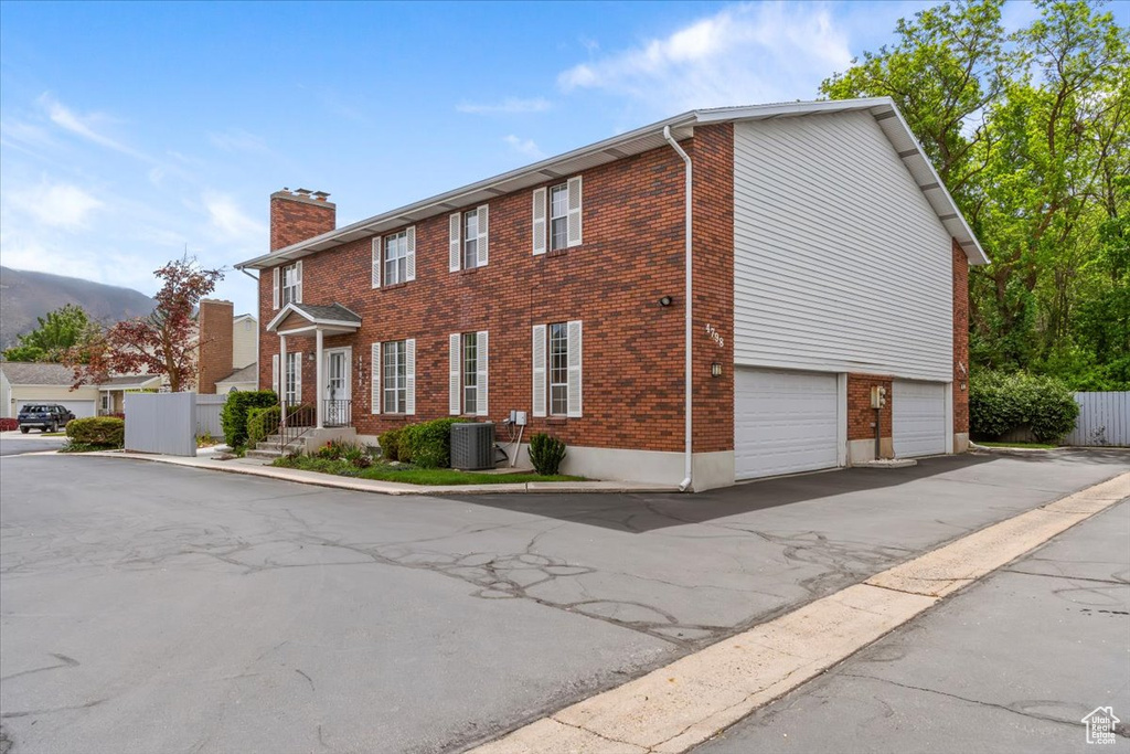 View of home\\\\\\\'s exterior featuring brick siding, a chimney, a garage, fence, and driveway