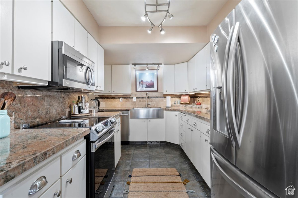 Kitchen featuring stainless steel appliances, a sink, decorative backsplash, and white cabinetry