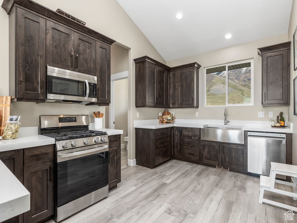 Kitchen featuring lofted ceiling, dark brown cabinets, light countertops, a sink, and appliances with stainless steel finishes