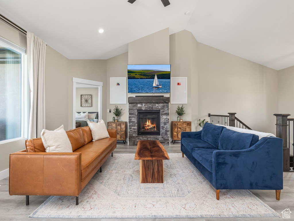 Living room with ceiling fan, a fireplace, vaulted ceiling, and light wood finished floors