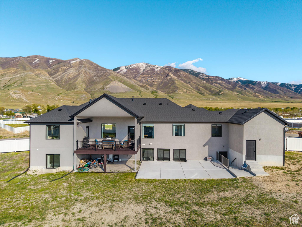 Back of house with a lawn, a mountain view, stucco siding, and a patio area