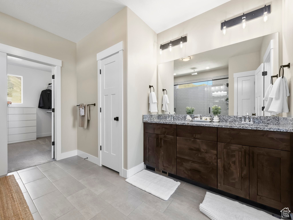Bathroom with double vanity, a walk in closet, a shower stall, a sink, and baseboards