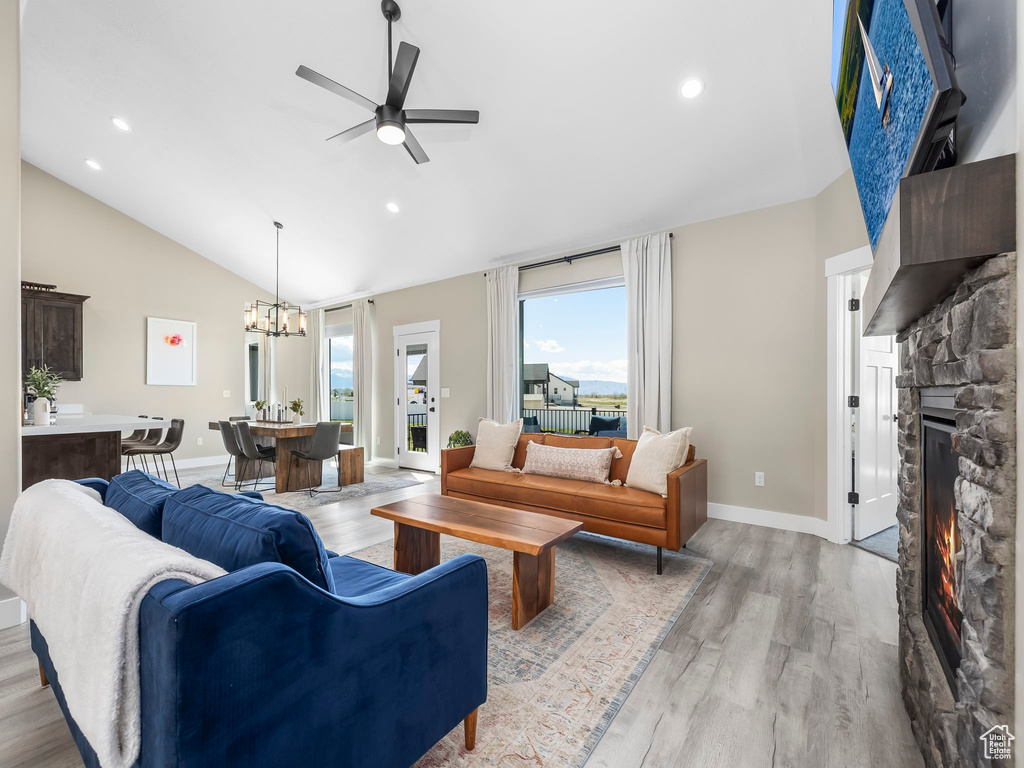 Living area with a fireplace, ceiling fan with notable chandelier, baseboards, lofted ceiling, and light wood-type flooring