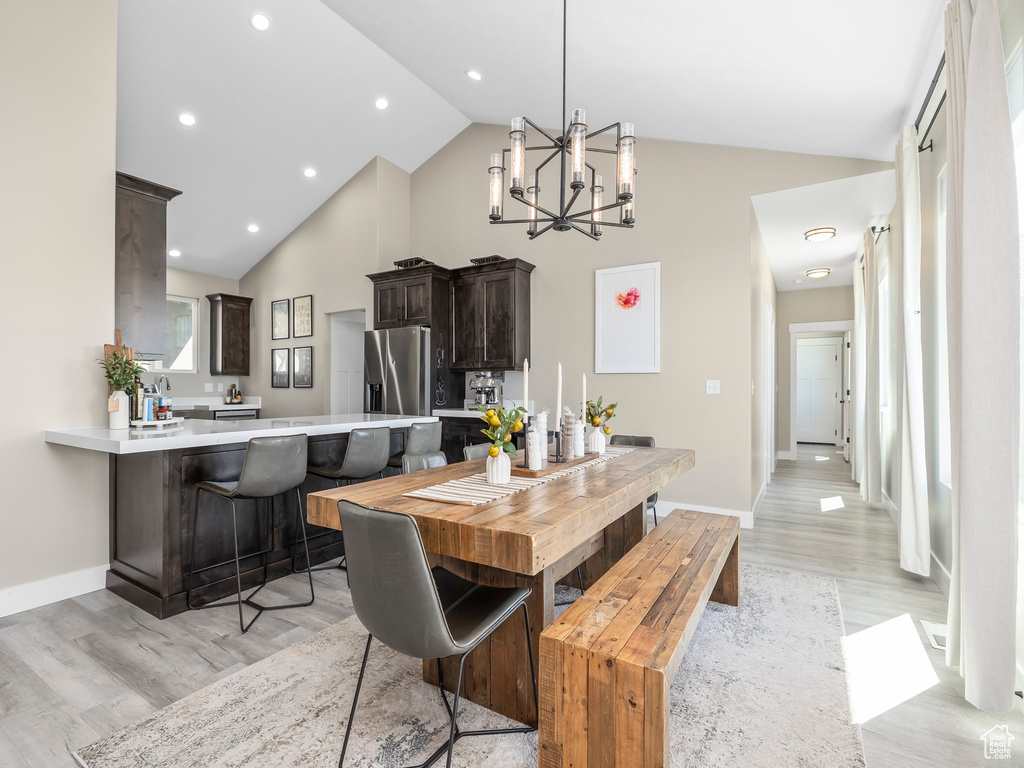 Dining room featuring high vaulted ceiling, a notable chandelier, baseboards, and light wood-type flooring
