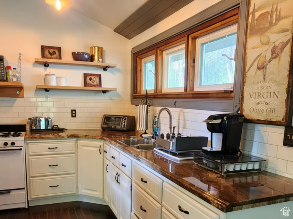 Kitchen with white range with gas stovetop, tasteful backsplash, vaulted ceiling, dark wood-style floors, and white cabinetry