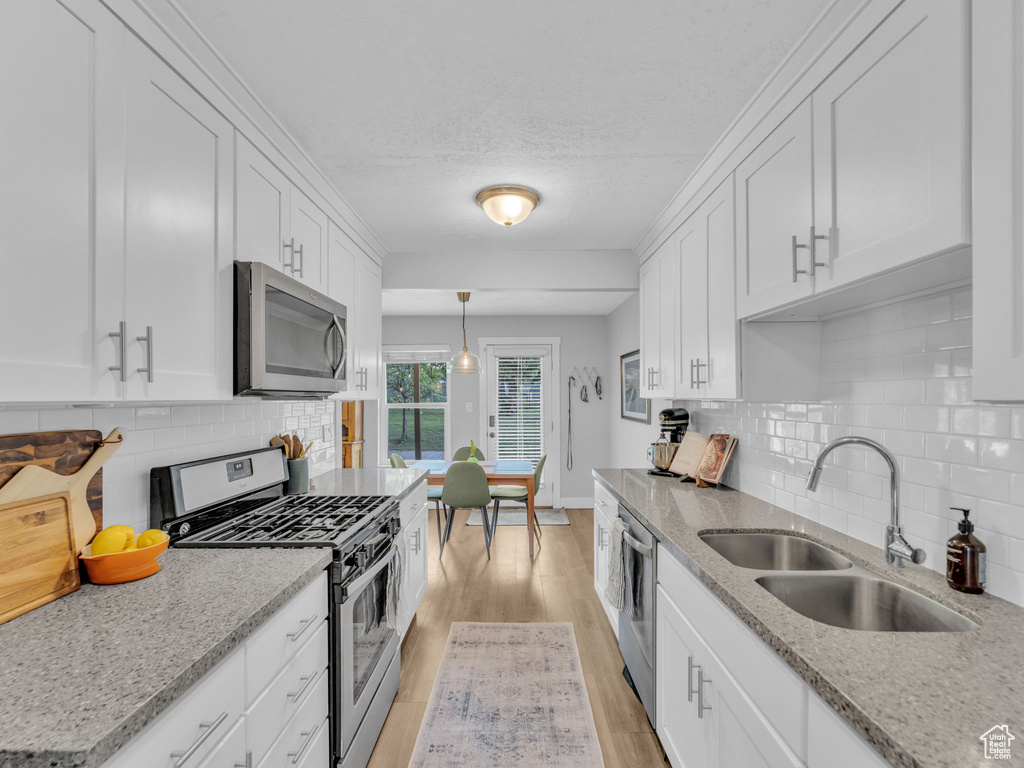 Kitchen featuring stainless steel appliances, a sink, light wood-style floors, white cabinets, and backsplash