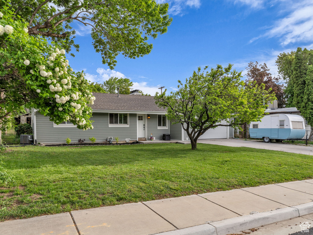 View of front of property with central AC, a front yard, driveway, and a garage