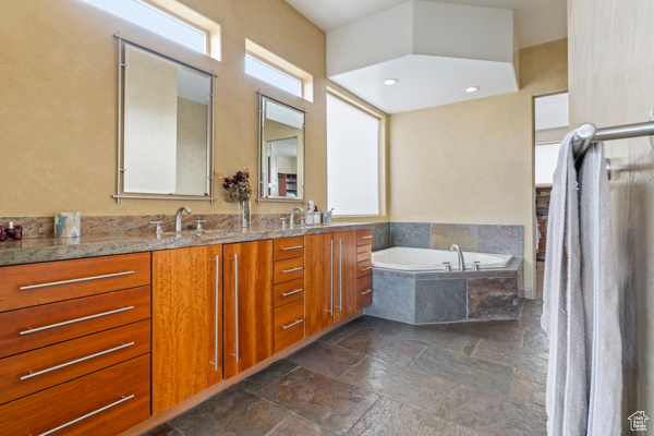 Bathroom featuring stone tile flooring, double vanity, and a garden tub