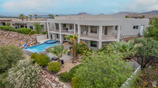 Rear view of property featuring stucco siding, a patio area, a pool with connected hot tub, and a balcony