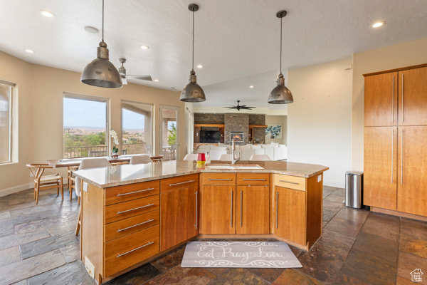 Kitchen with a sink, stone tile flooring, ceiling fan, pendant lighting, and open floor plan