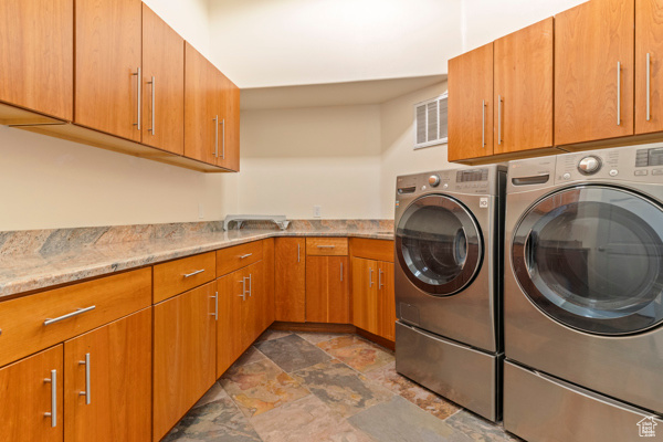 Washroom with dark stone finish flooring, cabinet space, and washing machine and clothes dryer