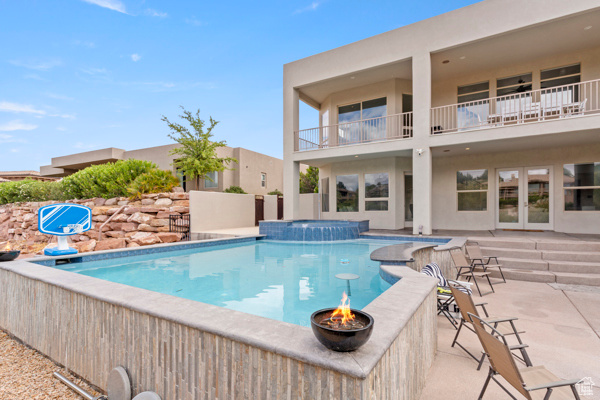 View of pool with an outdoor fire pit, a patio area, a pool with connected hot tub, and french doors