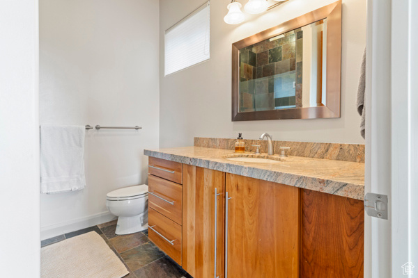 Full bathroom with vanity, stone tile floors, toilet, and baseboards