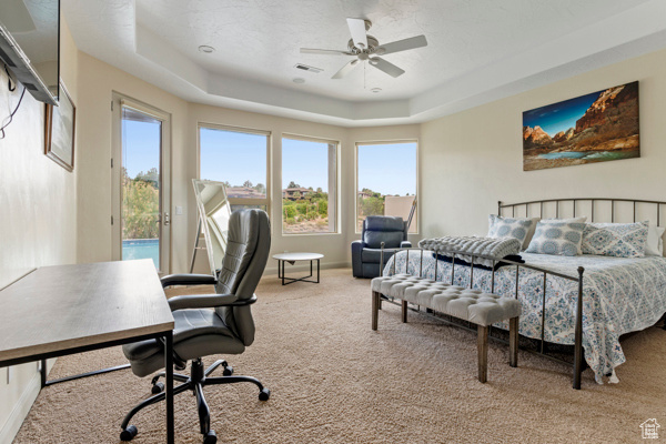 Carpeted bedroom with access to exterior, a tray ceiling, an office area, and ceiling fan