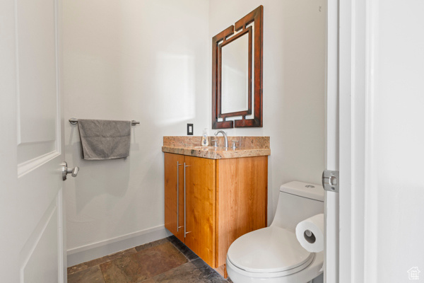 Bathroom with toilet, stone finish floors, vanity, and baseboards