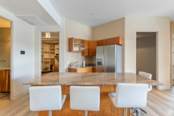 Kitchen featuring stainless steel refrigerator with ice dispenser, brown cabinets, light wood-type flooring, and baseboards