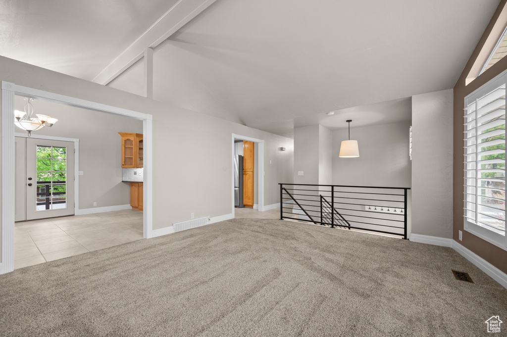 Empty room featuring light carpet, a chandelier, baseboards, and healthy amount of natural light