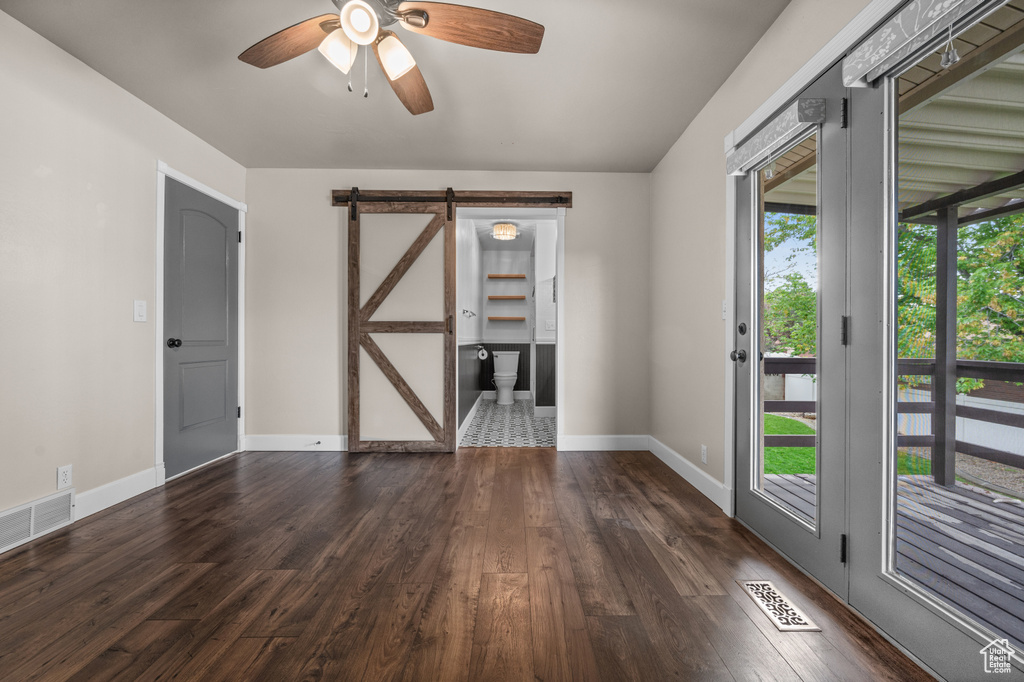 Empty room featuring a barn door, healthy amount of natural light, a ceiling fan, and wood finished floors
