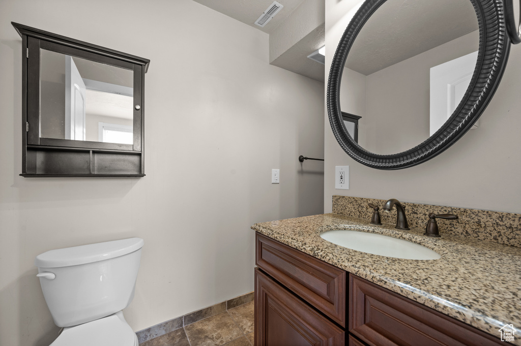 Half bath featuring baseboards, toilet, vanity, and stone finish floors