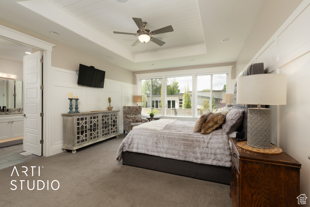 Carpeted bedroom featuring a raised ceiling, a decorative wall, connected bathroom, and a ceiling fan