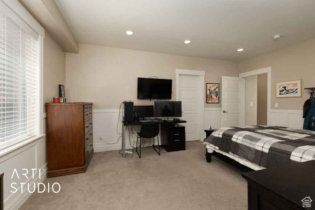 Bedroom featuring light colored carpet, a wainscoted wall, recessed lighting, a desk, and a decorative wall
