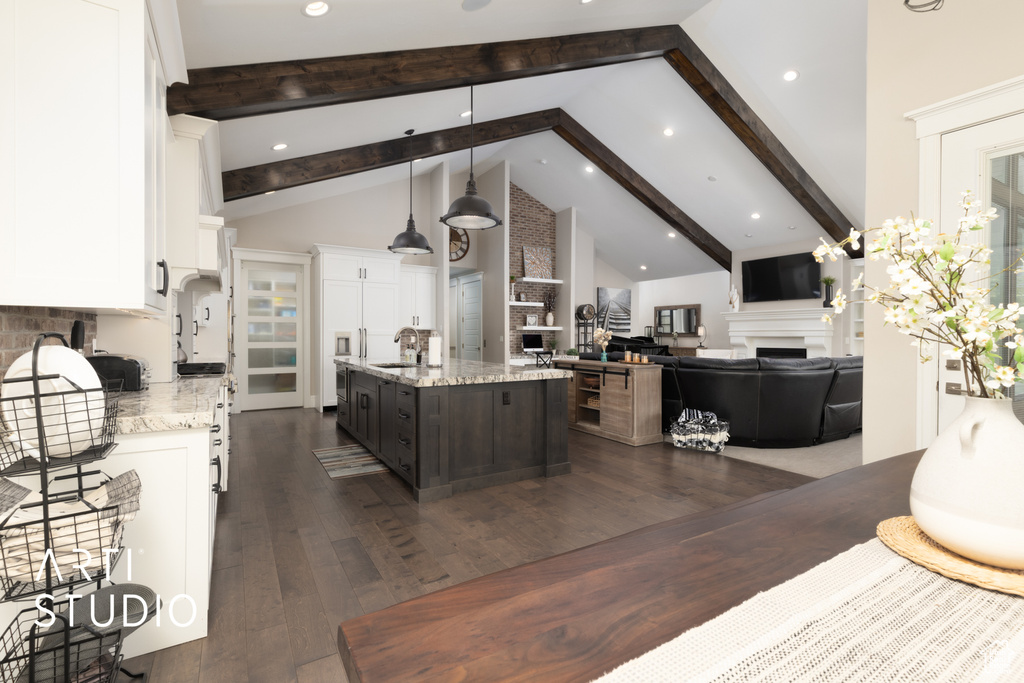 Kitchen with a fireplace, a sink, white cabinetry, an island with sink, and beam ceiling
