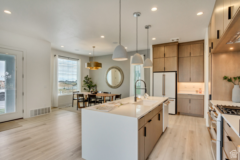 Kitchen with white appliances, a sink, light wood finished floors, light countertops, and hanging light fixtures