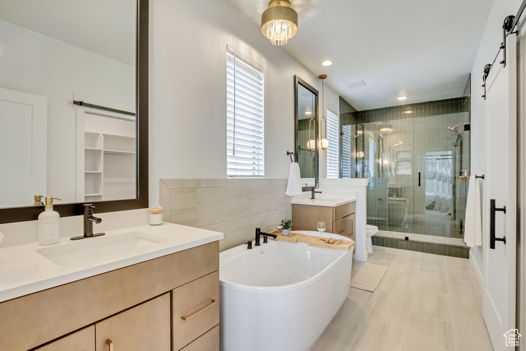Full bathroom with a shower stall, two vanities, toilet, a freestanding bath, and tile patterned flooring