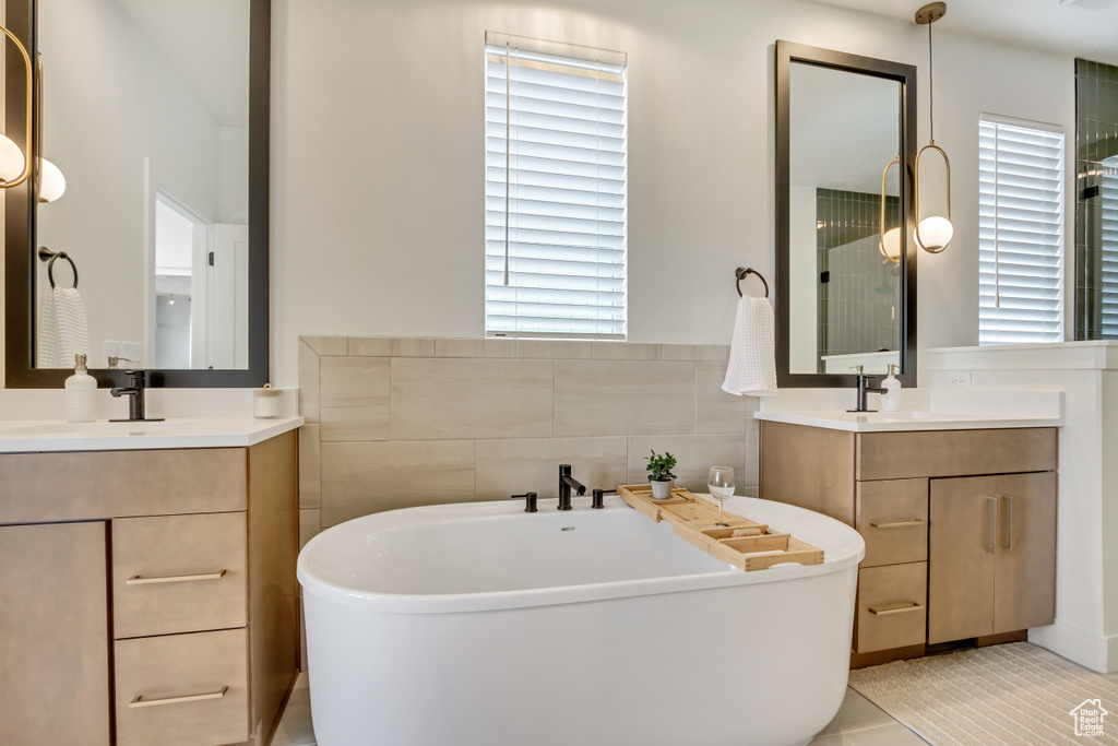 Full bathroom featuring healthy amount of natural light, a freestanding bath, two vanities, and tile patterned flooring