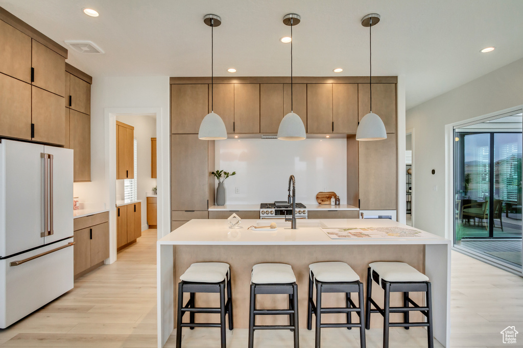 Kitchen featuring high end fridge, light wood-style flooring, a kitchen breakfast bar, recessed lighting, and light countertops