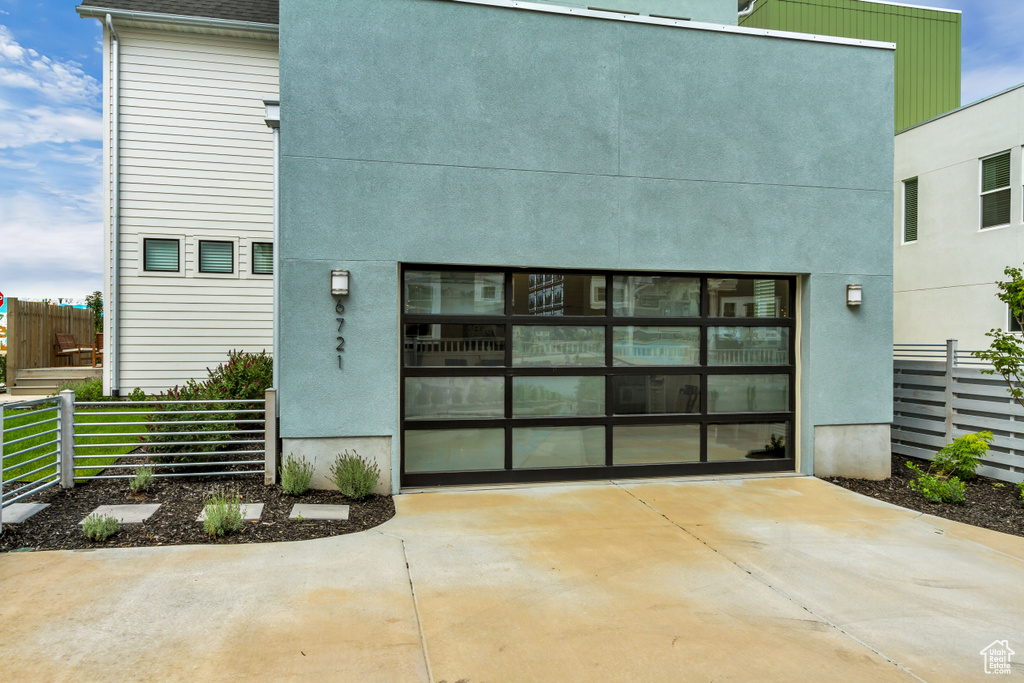 Back of property with fence, driveway, a garage, and stucco siding