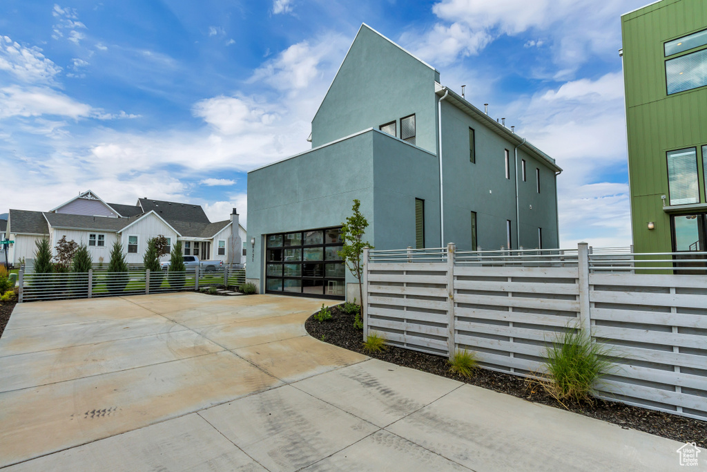 View of side of home with concrete driveway, fence, an attached garage, and stucco siding