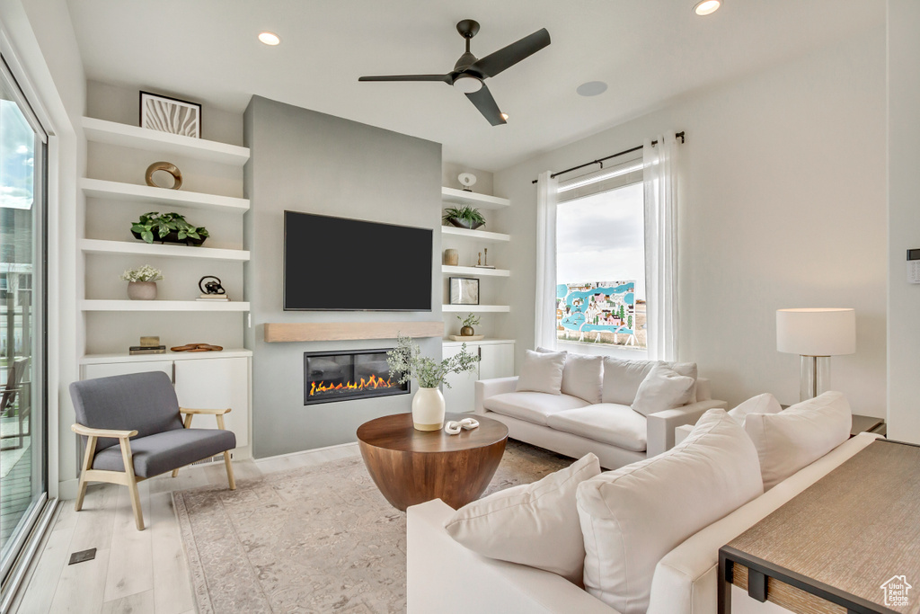 Living area with a ceiling fan, a glass covered fireplace, recessed lighting, and wood finished floors