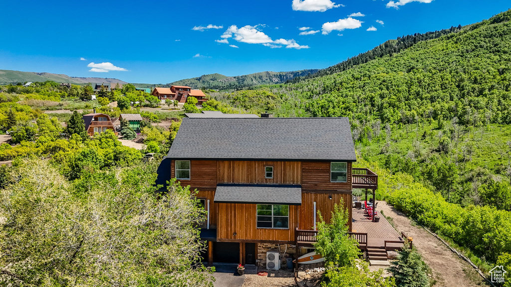 Rear view of property with roof with shingles, a wooded view, a deck with mountain view, a cooling unit, and a chimney