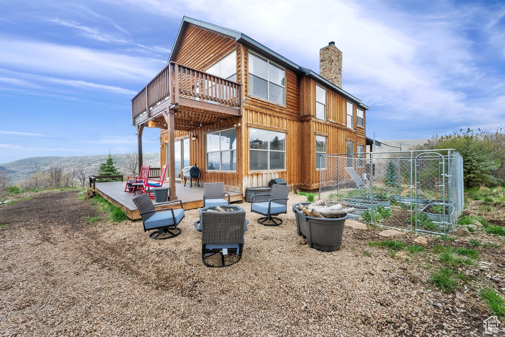 Rear view of property featuring a chimney, a wooden deck, board and batten siding, and a patio
