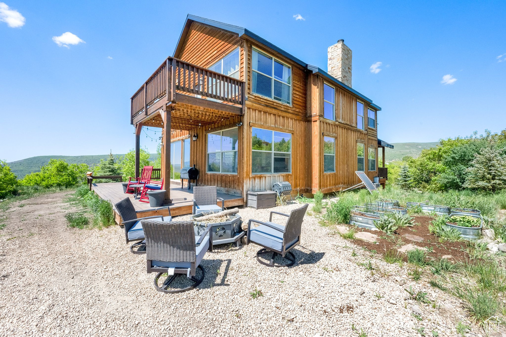 Rear view of house featuring an outdoor fire pit, a chimney, a vegetable garden, a deck, and board and batten siding