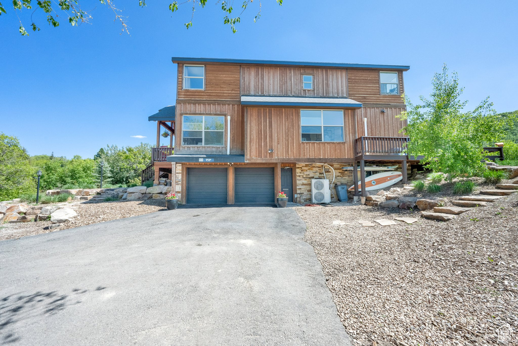 View of front of property with asphalt driveway, stone siding, stairs, and an attached garage
