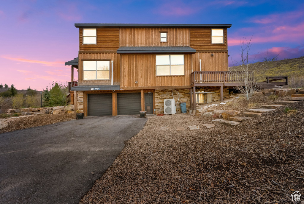 View of front facade with driveway, ac unit, stone siding, an attached garage, and a wooden deck