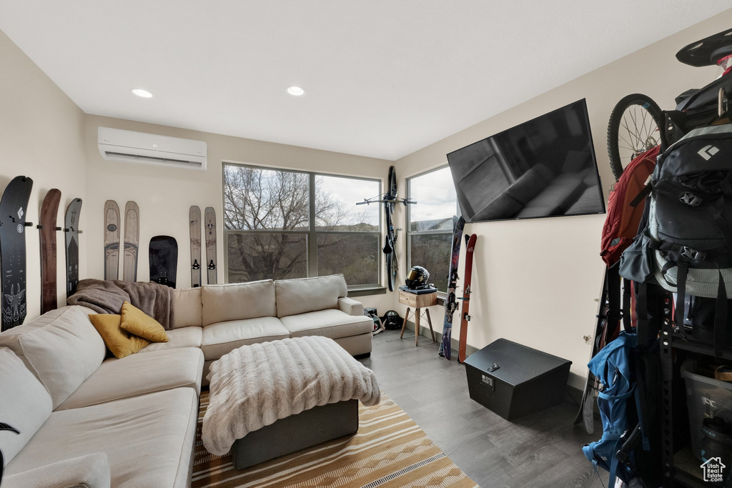 Living room with a wall unit AC, wood finished floors, and recessed lighting