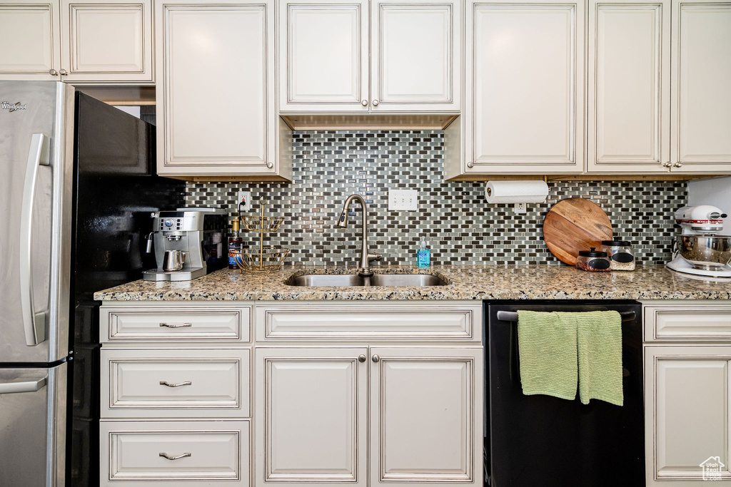 Kitchen featuring black dishwasher, a sink, tasteful backsplash, and white cabinets