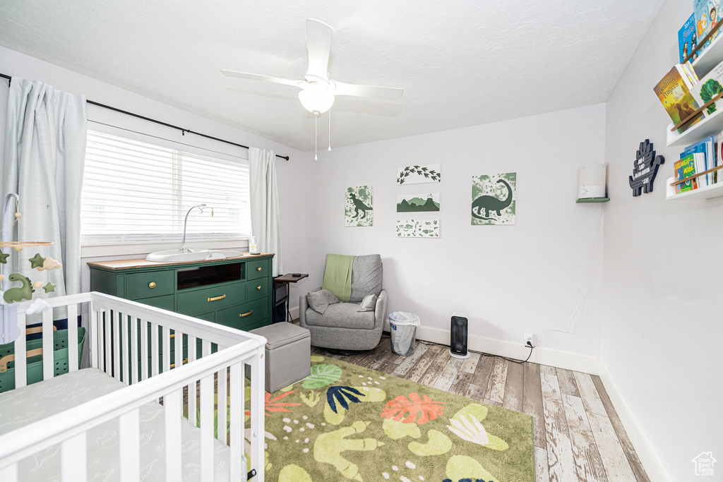 Bedroom featuring light wood-style flooring, a nursery area, baseboards, and a ceiling fan
