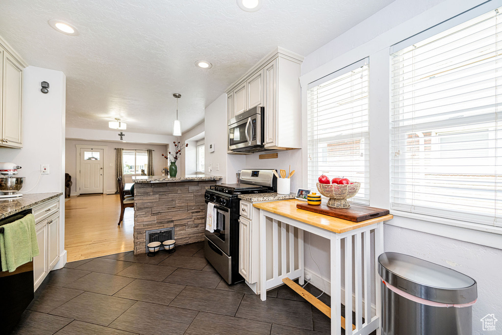 Kitchen featuring appliances with stainless steel finishes, a peninsula, recessed lighting, light stone countertops, and decorative light fixtures